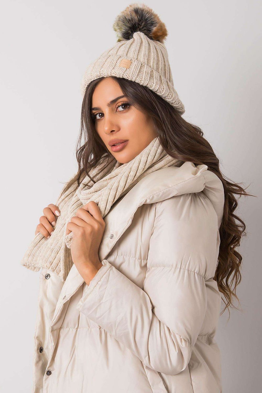 Elegant winter hat and scarf set styled with a plush pom pom, modelled by a woman in a chic coat for luxurious cold weather fashion.