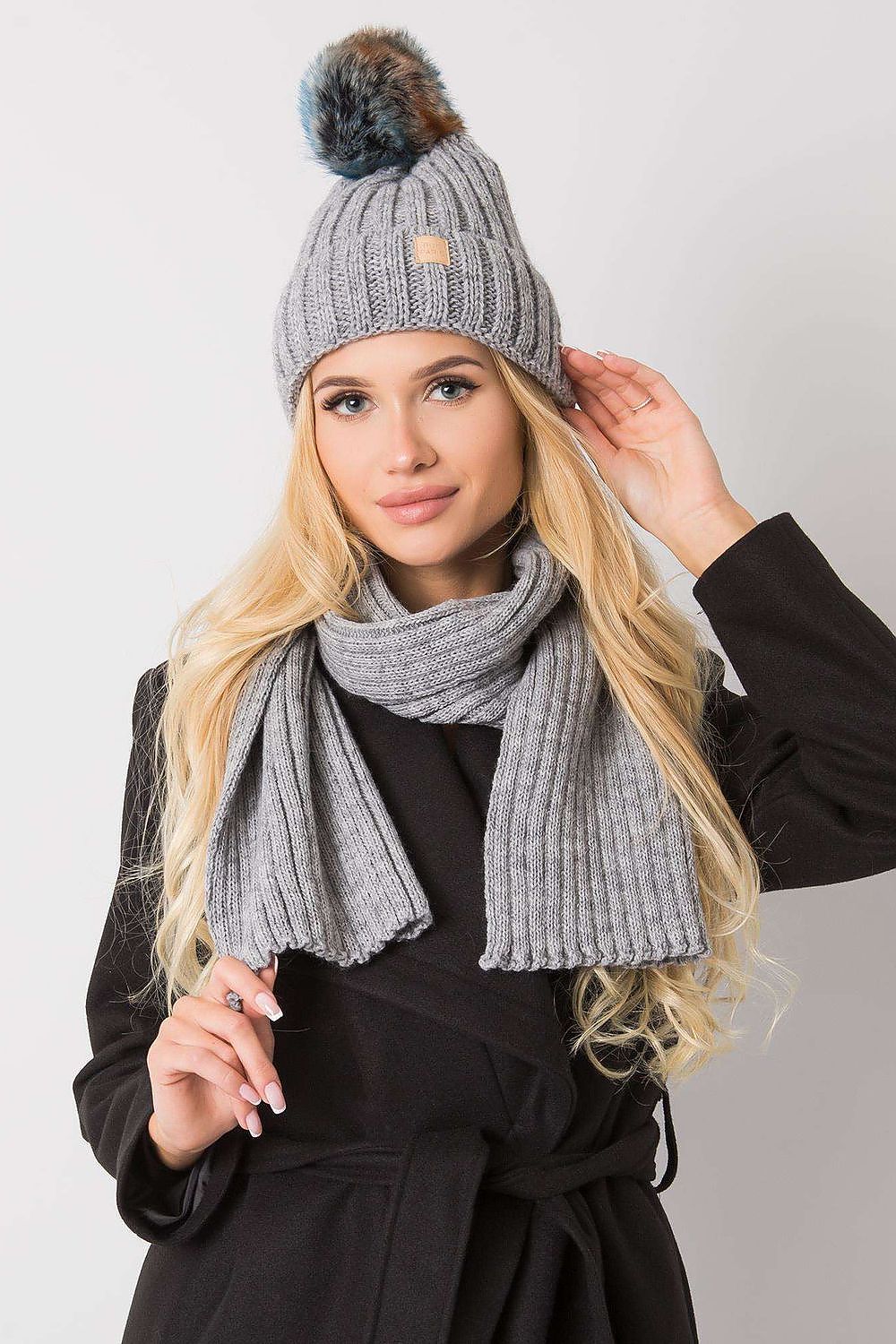 Luxurious grey winter hat adorned with a pom pom and paired with a matching scarf, elegantly modelled by a woman, ideal for fashionable winter looks.