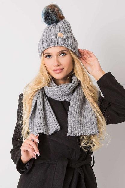 Luxurious grey winter hat adorned with a pom pom and paired with a matching scarf, elegantly modelled by a woman, ideal for fashionable winter looks.