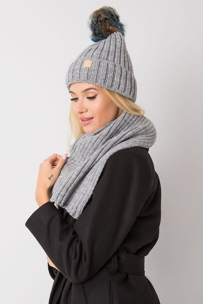 Sophisticated winter outfit featuring a grey knitted hat and scarf set, modelled by a woman in a stylish coat, capturing a luxurious winter vibe.