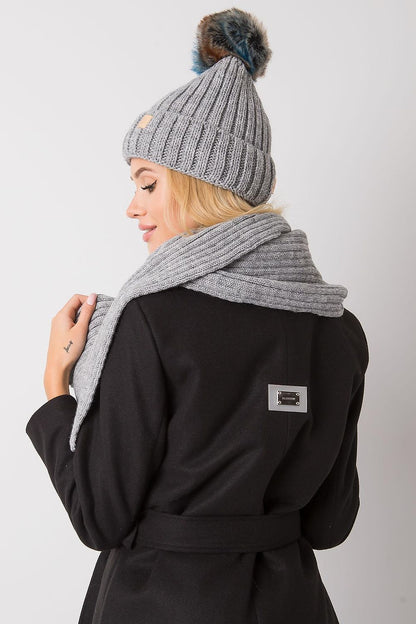 Winter fashion accessory set including a grey hat with a pom pom and a matching scarf, elegantly draped by a model for luxurious cold weather style.