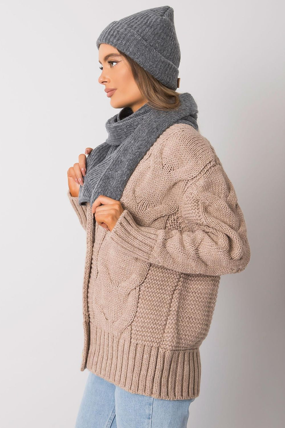 Profile view of a fashionable lady in a grey acrylic wool hat and matching scarf, complementing a stylish cable knit cardigan, perfect for cold weather outings.