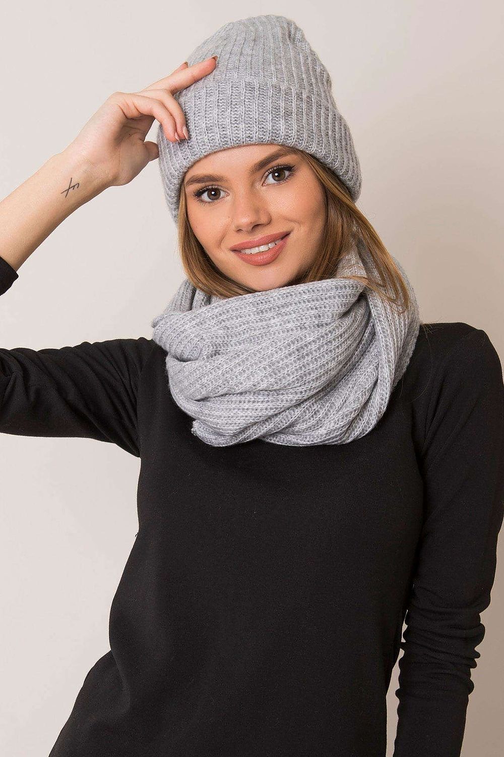 Elegant model wearing a light grey ribbed knit hat and oversized scarf, radiating warmth and luxury against a minimal background, perfect for winter fashion.