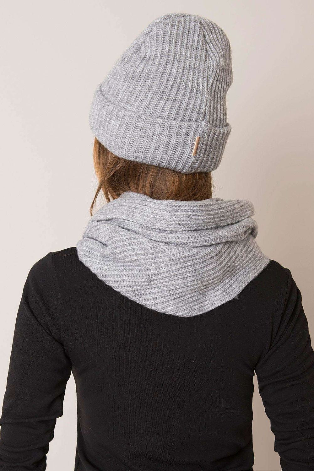 Back view of a stylish woman wearing an elegant grey knitted winter set, featuring a soft acrylic and wool blend hat and scarf, perfect for winter sophistication.