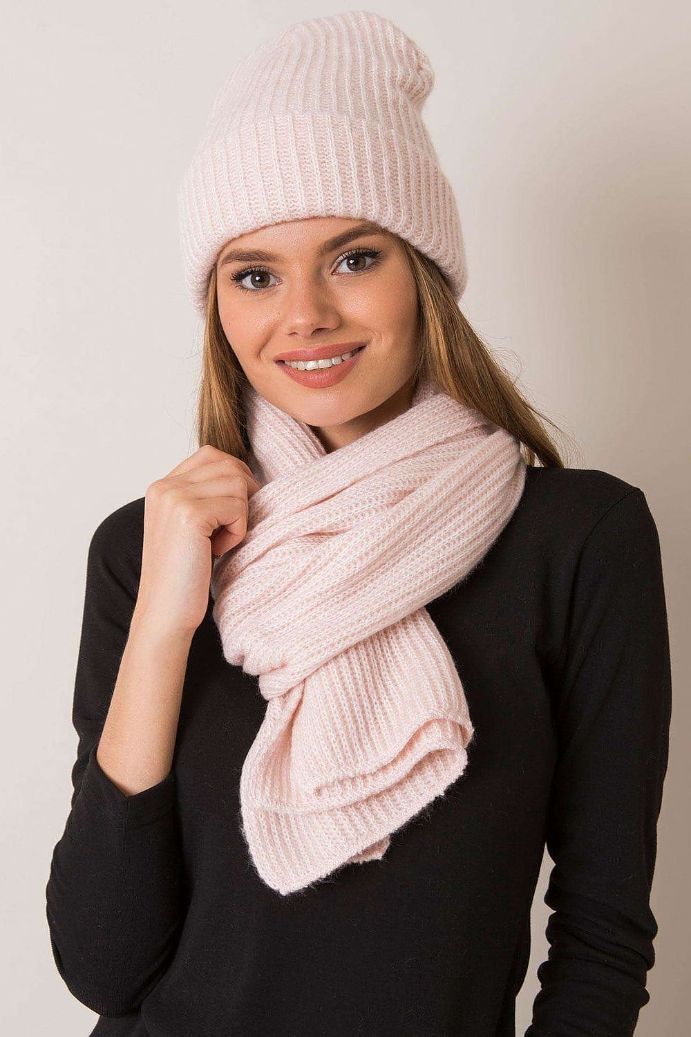 Smiling woman showcasing a luxurious pink knitted winter set, including a chic beanie and scarf, highlighting the soft texture ideal for fashionable winter outings.