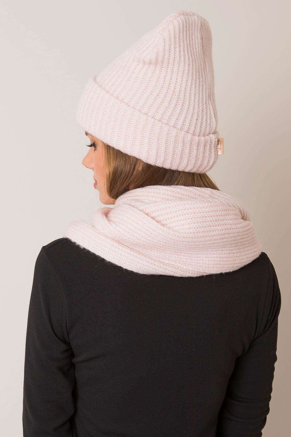 Side view of a fashionable woman modeling a beautiful pink knitted hat and scarf set, designed for ultimate warmth and elegance during the winter season.