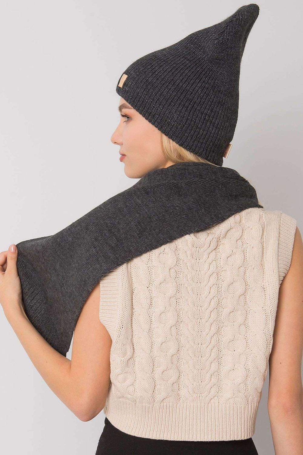 Elegant back view of a woman dressed in a luxurious dark grey beanie hat and scarf set, revealing a soft knit texture and fashionable silhouette for winter attire.