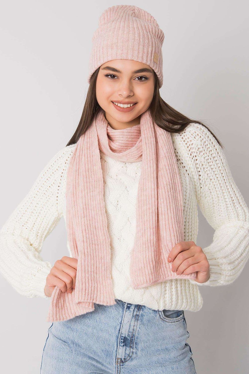 Luxurious 100% acrylic winter hat and scarf set by Rue Paris, elegantly modelled. The soft pink knit hat and matching scarf showcase a refined ribbed texture, complemented by a cozy white cable-knit sweater.