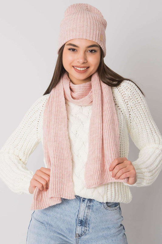 Luxurious 100% acrylic winter hat and scarf set by Rue Paris, elegantly modelled. The soft pink knit hat and matching scarf showcase a refined ribbed texture, complemented by a cozy white cable-knit sweater.
