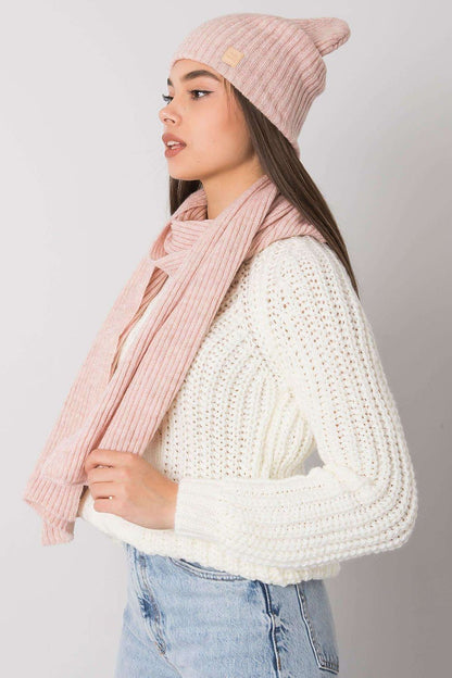 Side view of a model showcasing a luxurious pink acrylic winter hat and scarf set by Rue Paris. The elegant ribbed design adds a stylish touch against a backdrop of a cozy white cable-knit sweater.
