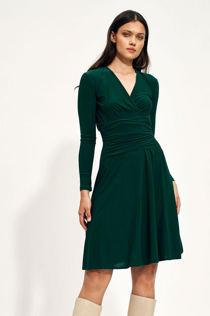 Luxurious green midi dress showcasing an enveloping neckline and fitted waist, complemented by stylish knee-high boots, perfect for autumn soirées.