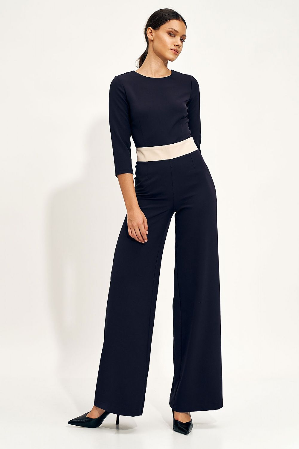 Chic navy blue jumpsuit featuring a fitted bodice and voluminous wide-leg trousers, model poses gracefully highlighting the design's elegance.