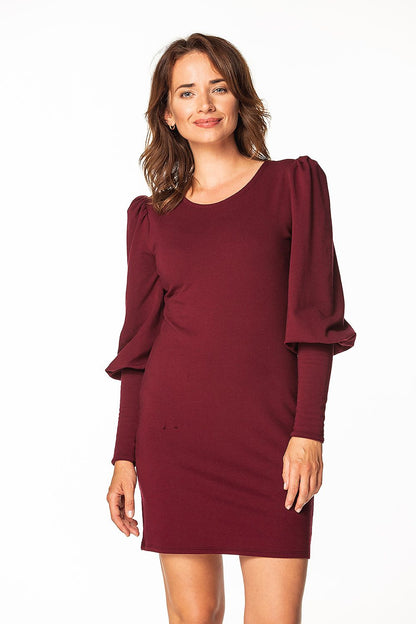 Elegant woman modelling a luxury knitted mini dress with boat neckline and long buffed sleeves by Tessita, featuring a rich burgundy colour.
