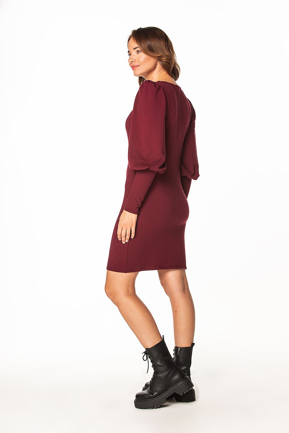 Sophisticated view of a woman in a luxury knitted mini dress by Tessita, featuring an elegant boat neckline and voluminous sleeves in a deep burgundy shade.