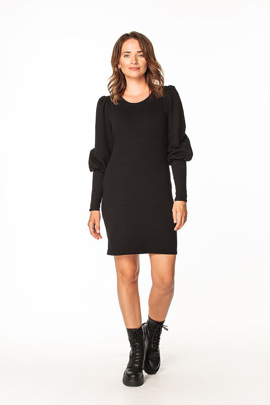 Chic model posing in the Tessita luxury knitted mini dress with a boat neckline and voluminous long sleeves, complemented by stylish black ankle boots, embodying a modern luxury aesthetic.