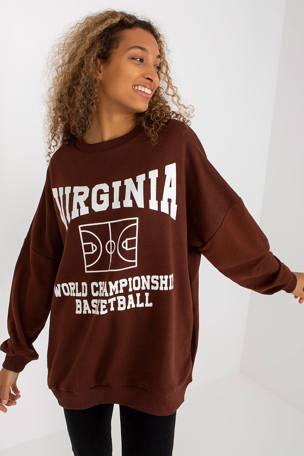 Chic women's long-sleeved cotton sweatshirt in stunning brown, adorned with a bold basketball-themed print stating 'WORLD CHAMPIONSHIP BASKETBALL.' Model poses gracefully, highlighting the stylish and relaxed oversized silhouette with practical side pockets.