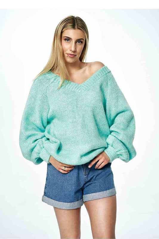 Elegant woman wearing a luxurious mint green Figl deep V-neck sweater with wide sleeves, paired with denim shorts, exuding a stylish and trendy vibe.