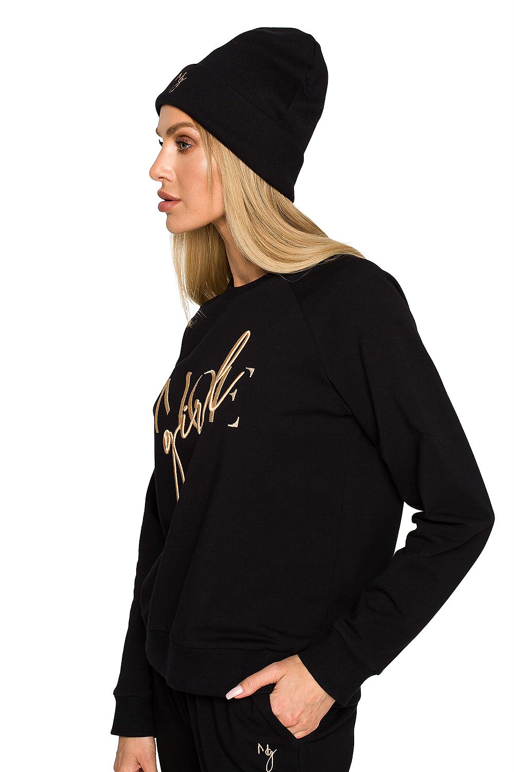 Side view of a stylish woman in a black ribbed knit beanie and matching sweatshirt, embodying sophisticated autumn fashion with delicate embroidered details.