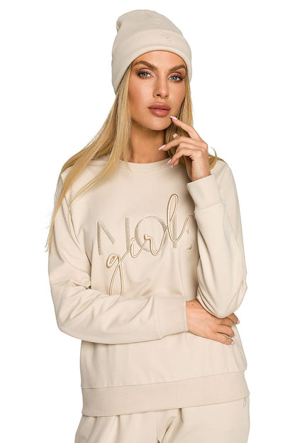 Elegant female model in a cream ribbed knit cap with intricate embroidery, radiating sophistication while posing in a matching sweatshirt.