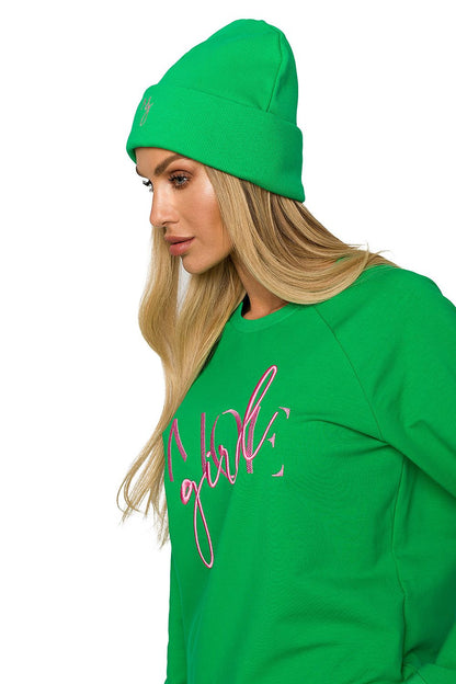 Profile view of a fashionable woman wearing a green ribbed knit cap adorned with delicate embroidery, paired with a stylish green sweatshirt, highlighting her trendy ensemble.