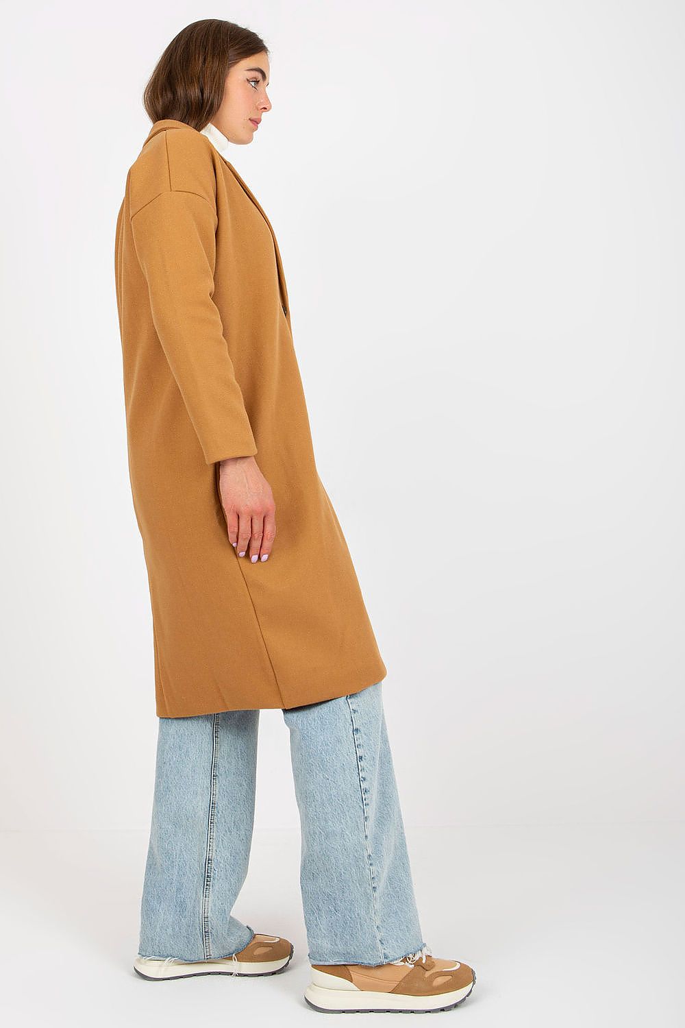Side view of an elegant camel luxury women's single-breasted coat, paired with flared jeans, emphasizing its modern aesthetic and comfortable fit.
