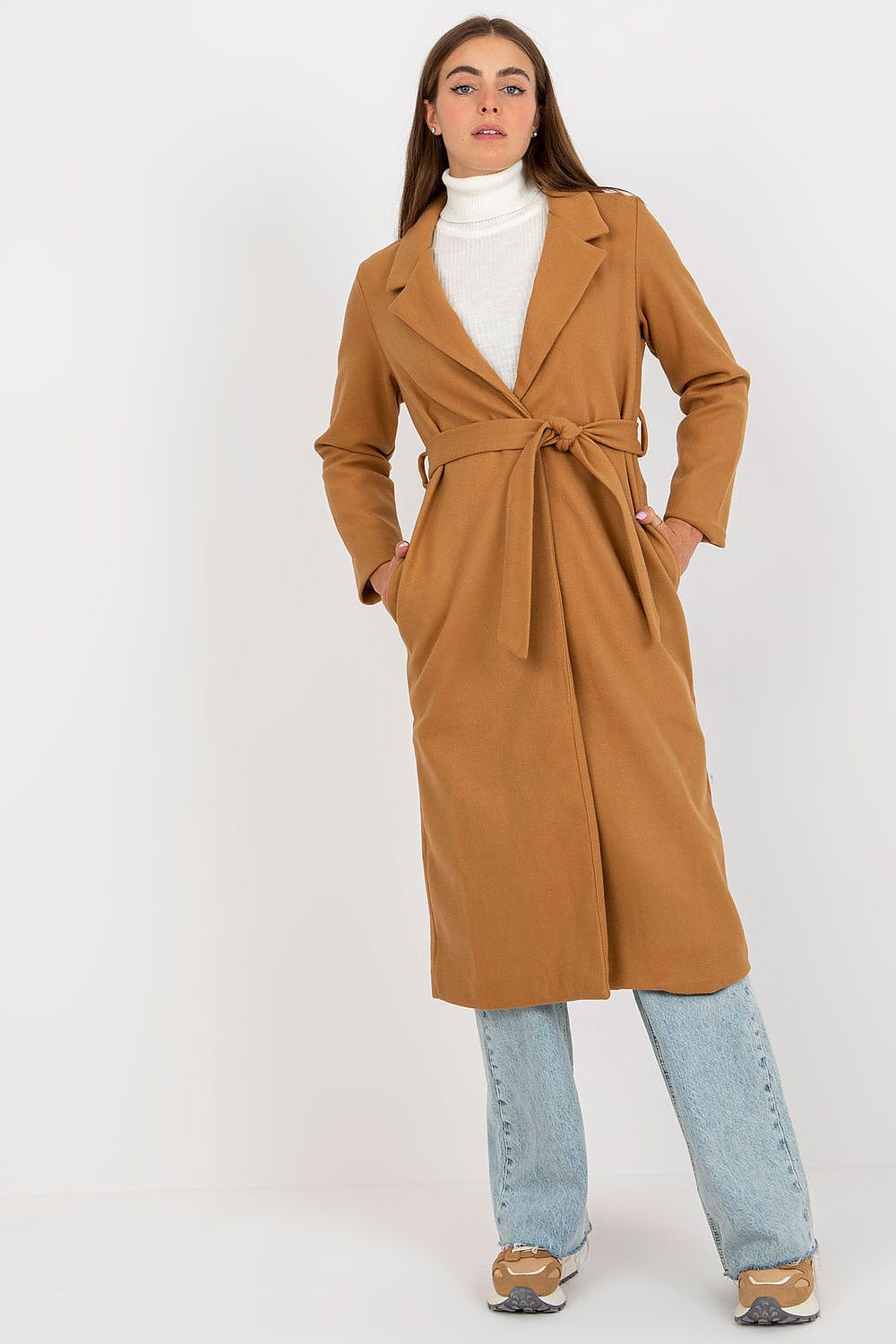 Elegant woman wearing a chic ochre long-sleeve coat with a tie belt and slip pockets, paired with a white turtleneck and light blue jeans, showcasing modern fashion sophistication.