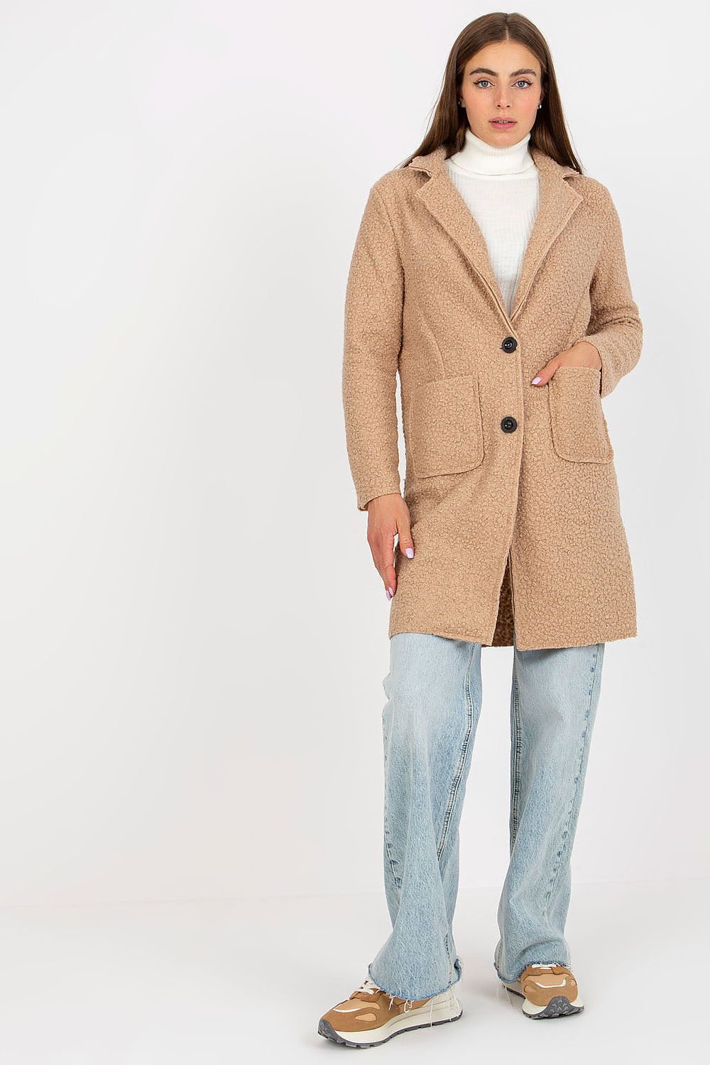 Fashionable view of the Och Bella luxury women's unlined coat in beige, with button detailing and patch pockets, elegantly worn with a white turtleneck and light blue relaxed fit jeans.
