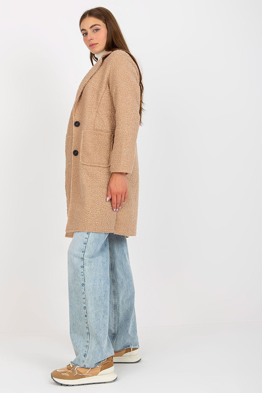 Side profile of the Och Bella luxury women's beige unlined buttoned coat, styled with a sophisticated white turtleneck and oversized denim jeans, epitomising casual luxury fashion.