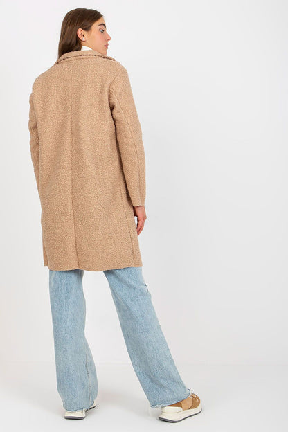 Elegant woman wearing an Och Bella luxury unlined buttoned coat in a soft beige hue, styled with long sleeves and patch slip pockets, paired with light denim pants and trendy sneakers, exuding a chic and sophisticated look.