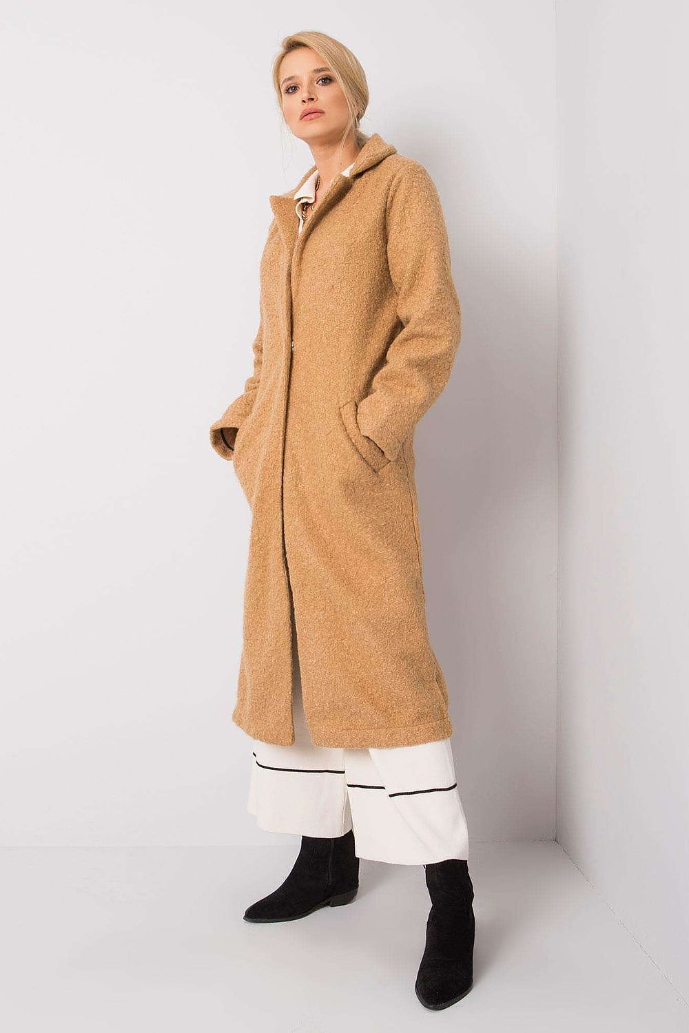 Luxurious Rue Paris women's long sleeve coat in a warm beige hue, featuring elegant press studs and practical side pockets, styled with chic black ankle boots.