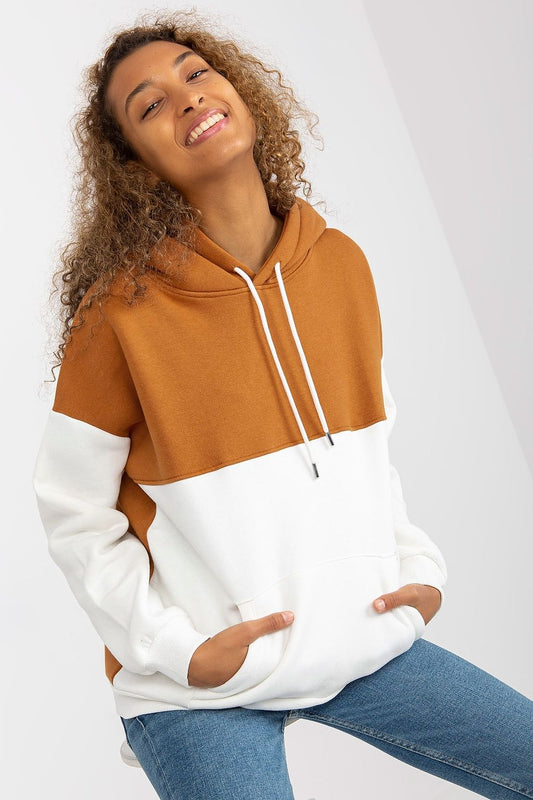 Luxurious women's sweatshirt by Rue Paris featuring a stylish two-color design with a hood and kangaroo pocket, model smiling with curls illuminated by natural light.