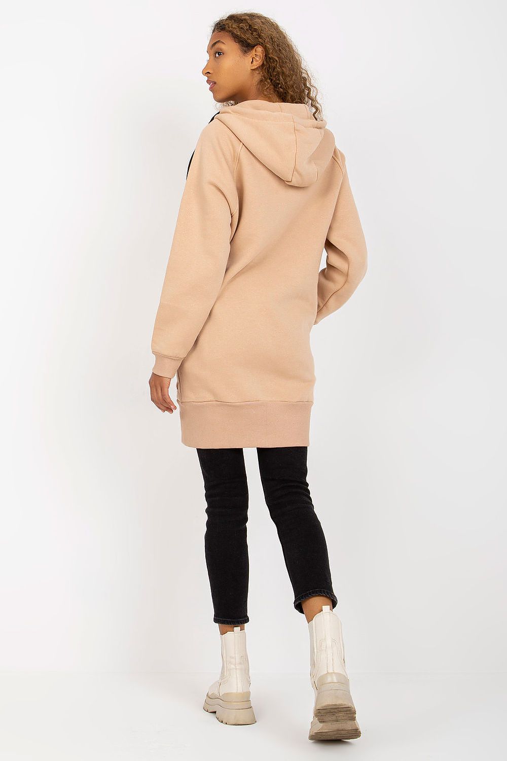 Back view of a luxury women’s hooded sweatshirt by Rue Paris in beige, designed with a long silhouette, zip detail, and cosy hood, perfectly paired with black skinny jeans and boots.