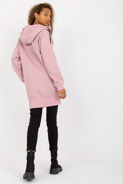 Back view of a luxury women’s pink hooded sweatshirt by Rue Paris showing the generous length, hood, and stylish design, beautifully complemented by fitted black jeans and ankle boots.