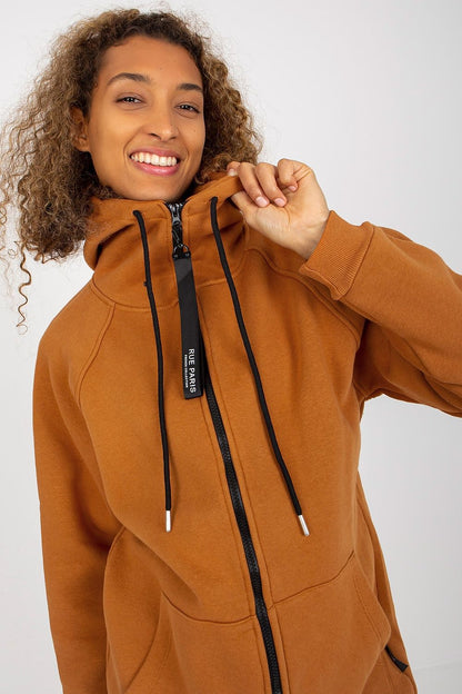 Close-up of a smiling model in a luxurious brown hooded sweatshirt by Rue Paris, featuring a zippered collar and sleek design, highlighting style and comfort in casual wear.