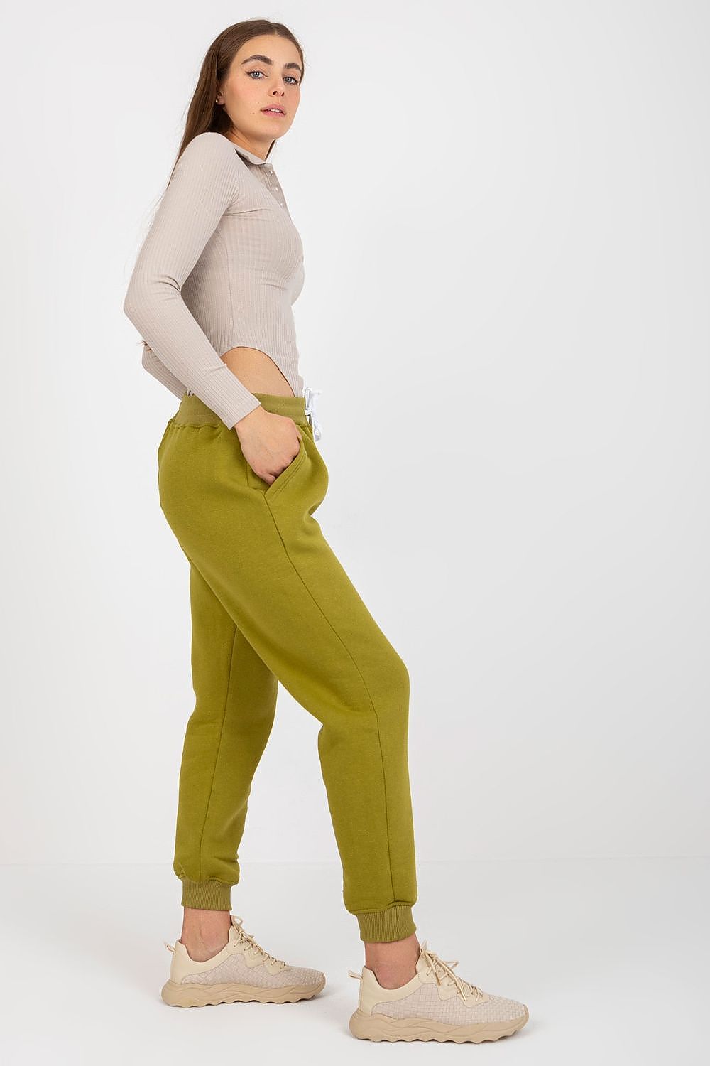 Side view of an elegant model wearing luxurious olive green cotton-spandex tracksuit trousers with waist tie and slip pockets, paired with a fashionable ribbed top.
