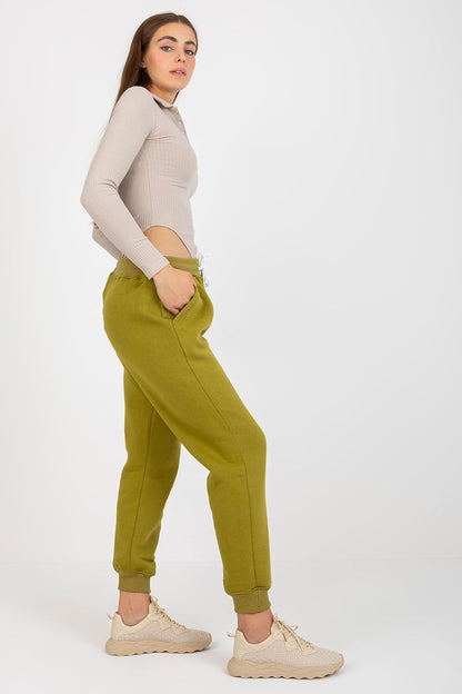 Side view of an elegant model wearing luxurious olive green cotton-spandex tracksuit trousers with waist tie and slip pockets, paired with a fashionable ribbed top.
