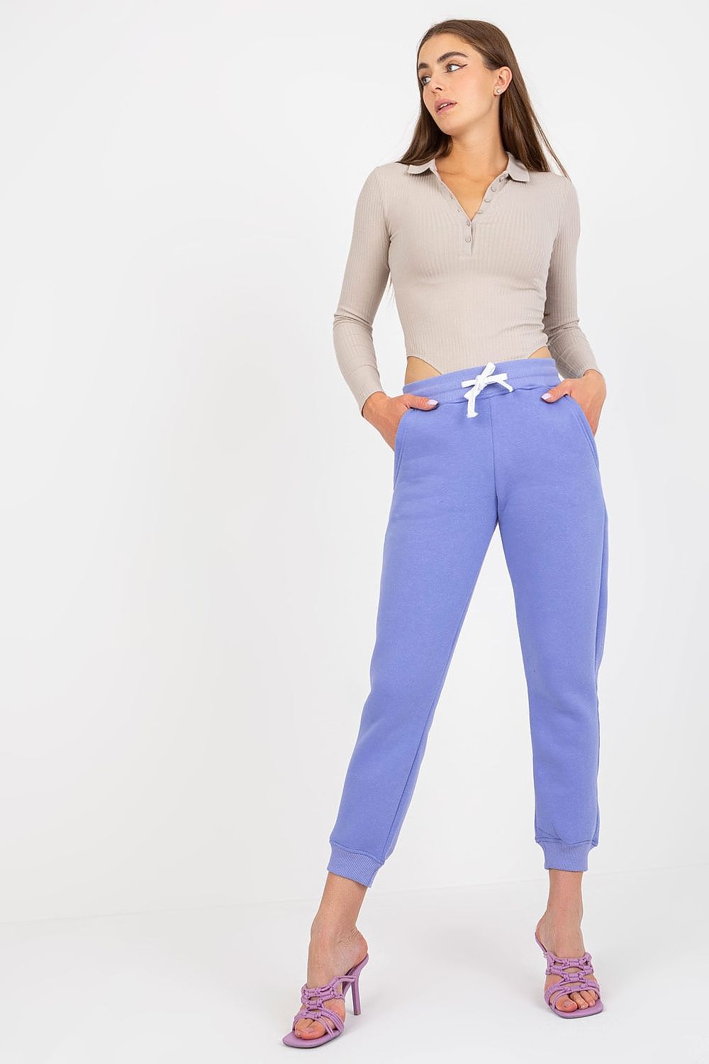 Stylish model in luxurious lavender cotton-spandex tracksuit trousers with waist tie and slip pockets, complemented by a fitted ribbed top and chic heels.