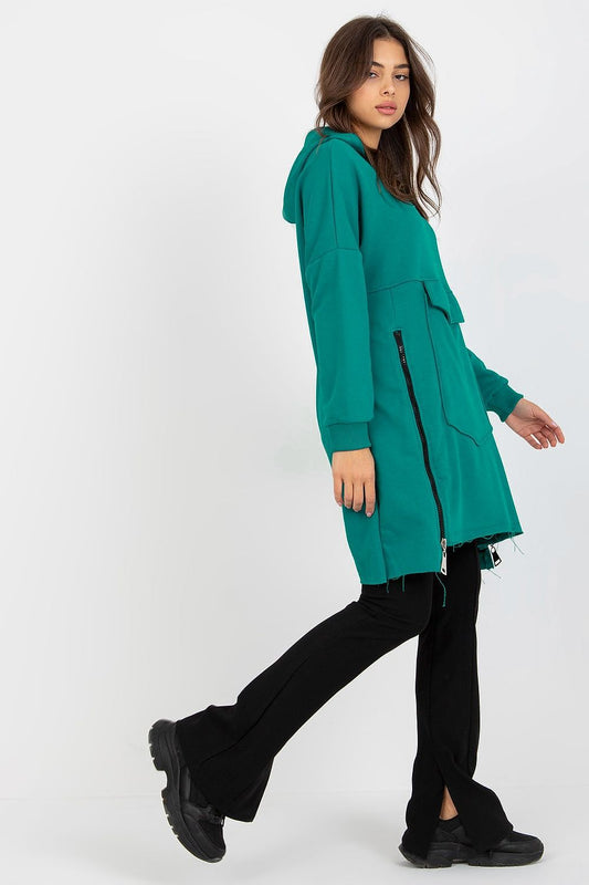 Chic turquoise extended cut sweatshirt with side zippers and large pocket, paired with stylish black pants.