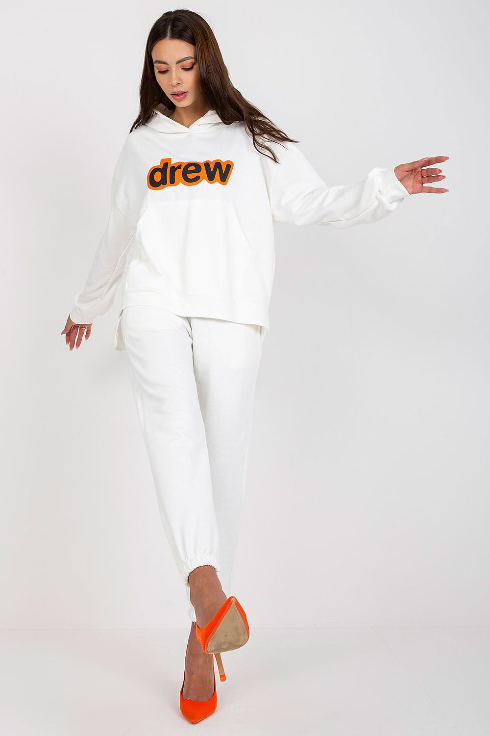 Elegant women’s luxe sweatshirt and pants ensemble in pristine white, adorned with contrasting orange logo, paired with striking orange high heels.
