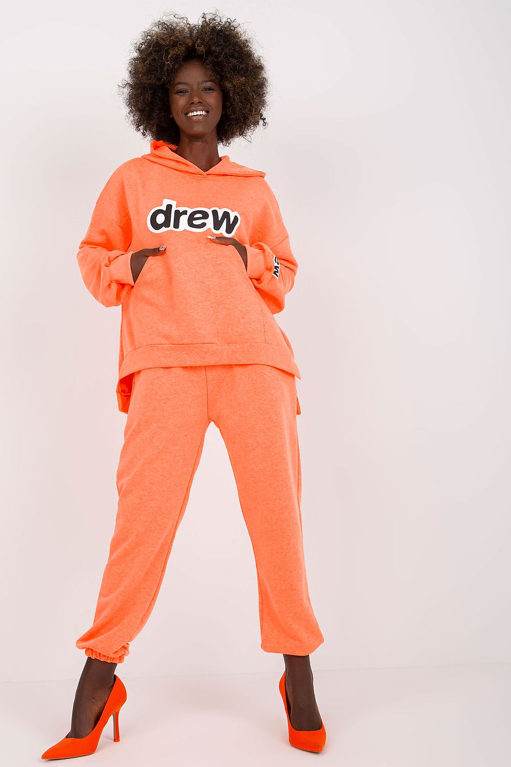 Chic and joyful representation of a luxe orange hoodie and pants set for women, accentuated with a prominent logo and sophisticated orange heels.