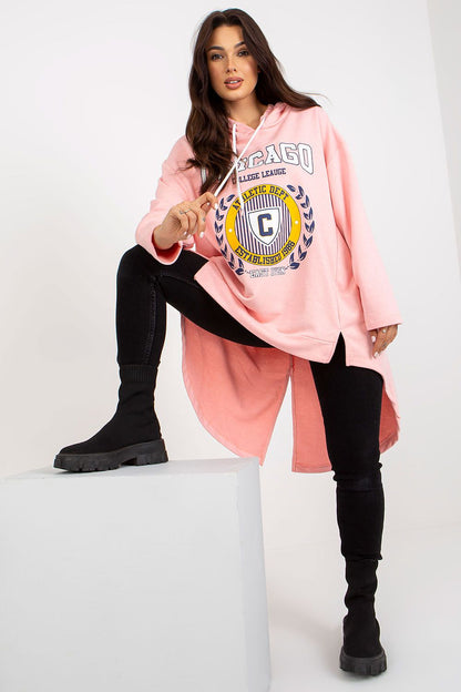 Stylish women's pink asymmetrical hoodie sweatshirt with long sleeves, featuring a college graphic print, paired with black skinny jeans and knee-high black boots, exuding a chic and relaxed vibe.