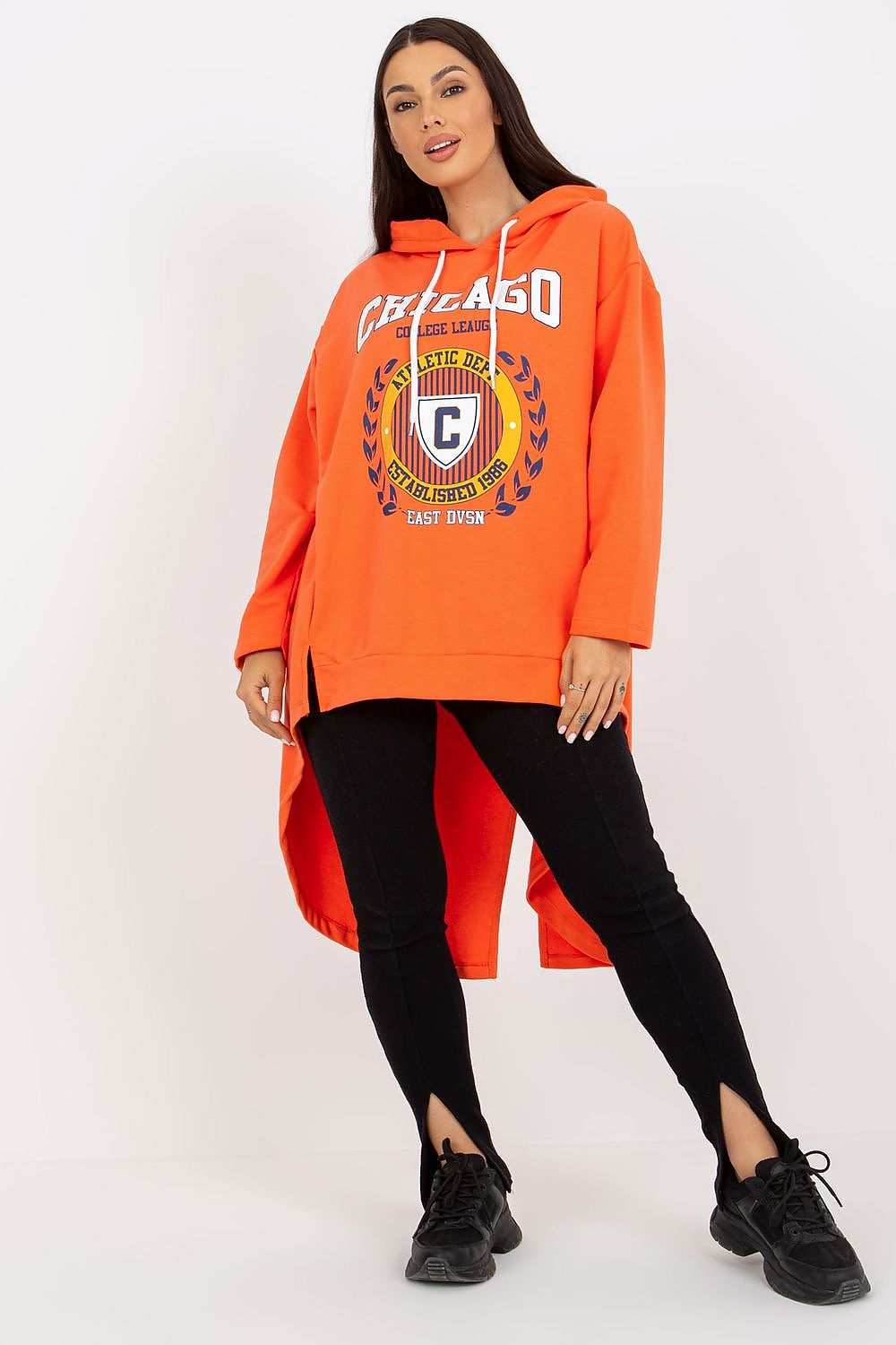 Front view of a vibrant orange asymmetrical hoodie sweatshirt worn by a stylish woman, effortlessly blending comfort and fashion, complemented by sleek black leggings and a confident demeanor.