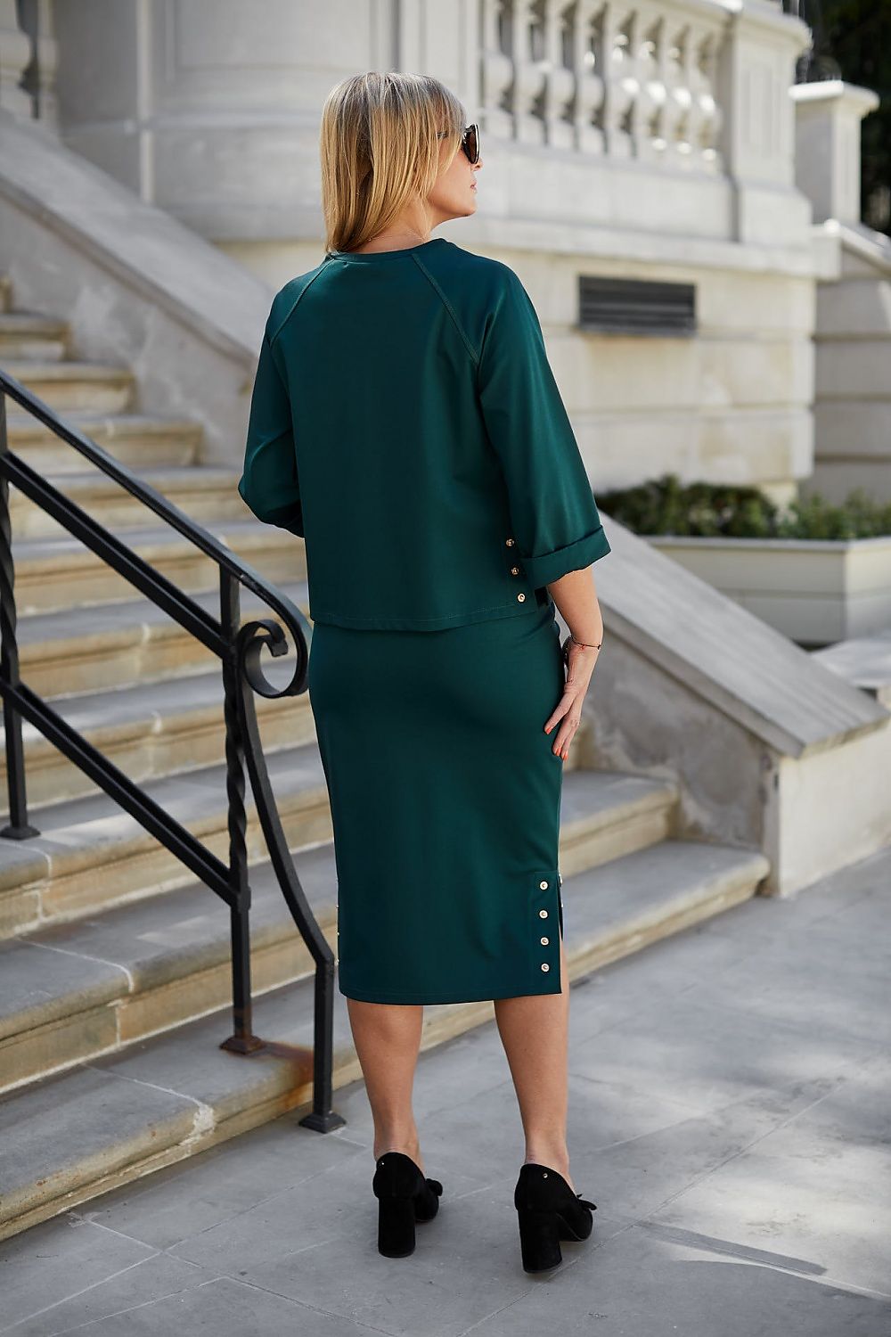 Back view of a woman in a luxurious Morgan knit two-piece set with stylish metallic press studs, exuding elegance as she stands on a staircase, highlighting the chic silhouette of the outfit.