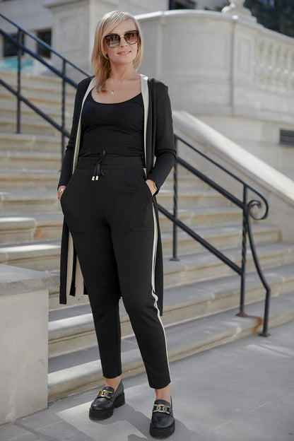 Elegant woman wearing the La Aurora Sporty Luxury Set, a soft viscose knit consisting of high waist pants and a chic loose blouse, accessorized with sunglasses, standing confidently on stairs.