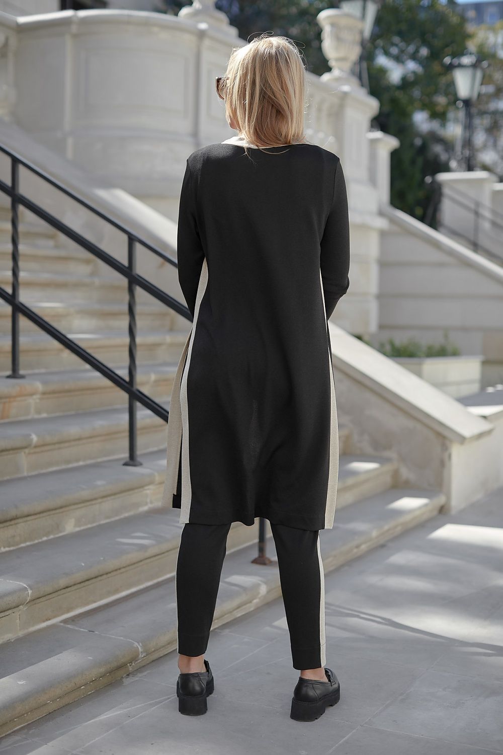 Back view of an elegant woman showcasing the La Aurora Sporty Luxury Set, featuring high waist pants and a stylish loose blouse, highlighting the luxurious fabric and sophisticated design against an outdoor staircase backdrop.