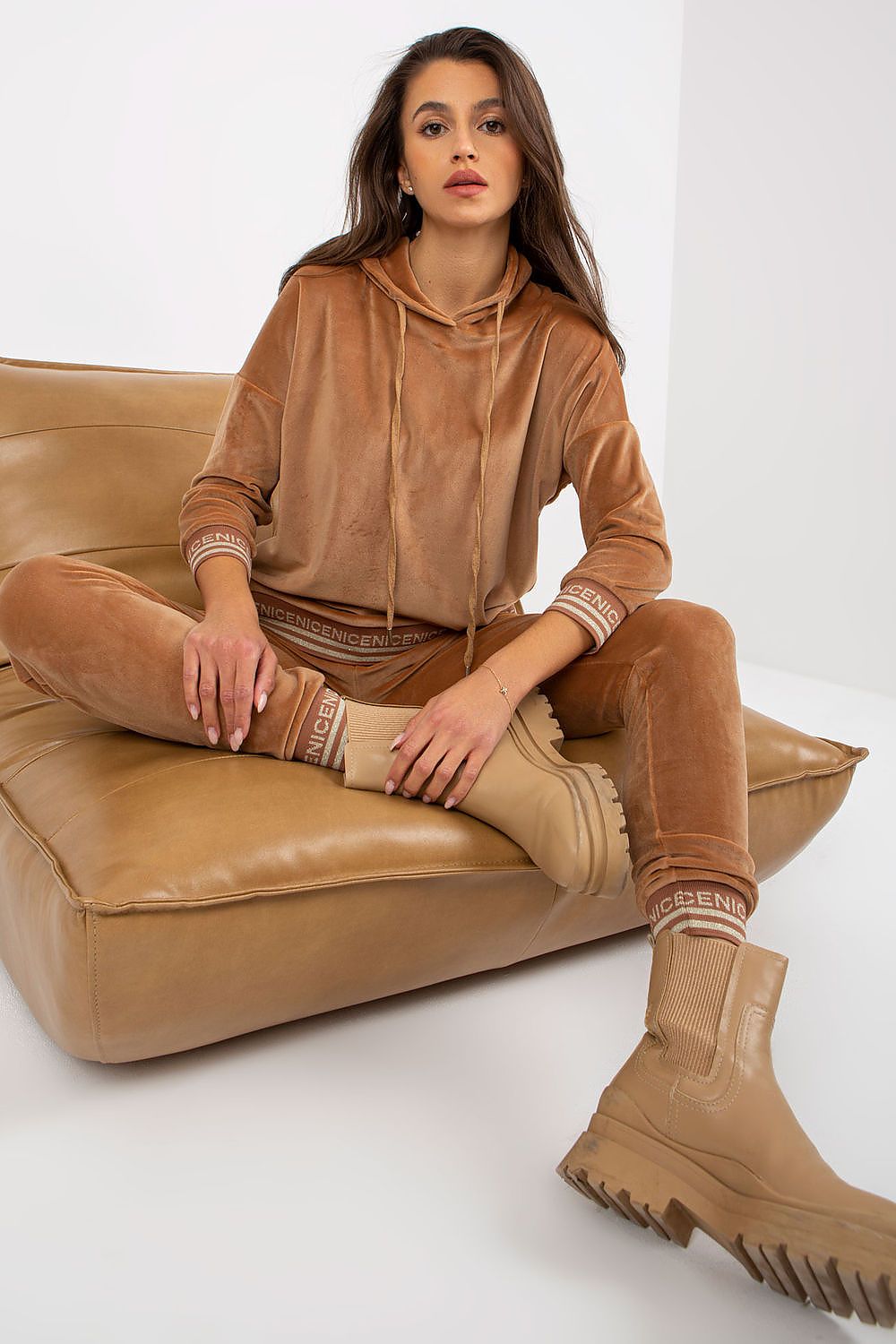 Fashionable women's velour set in a warm beige tone, featuring a hooded top and matching pants, styled with chic boots for a modern luxury aesthetic.