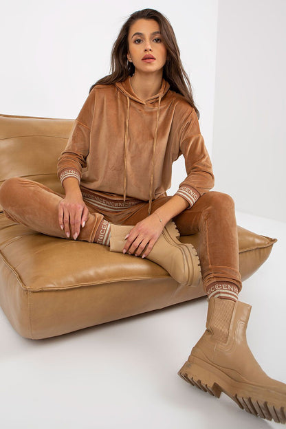 Fashionable women's velour set in a warm beige tone, featuring a hooded top and matching pants, styled with chic boots for a modern luxury aesthetic.
