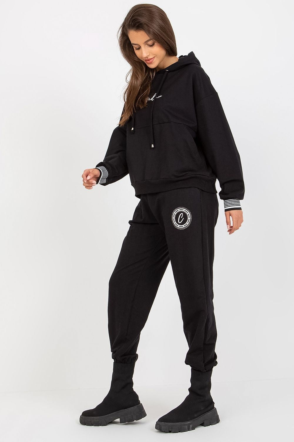 Luxury cotton blend sweatshirt and pants set in black, featuring a comfortable hood, kangaroo pocket, and adjustable waist tie. Model showcasing a chic athleisure look with stylish black boots.