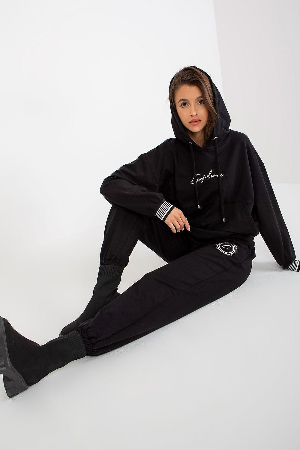 Sophisticated woman reclining stylishly in a luxury black cotton blend sweatshirt and trousers set, featuring a kangaroo pocket and adjustable waist tie, exuding comfort and elegance.