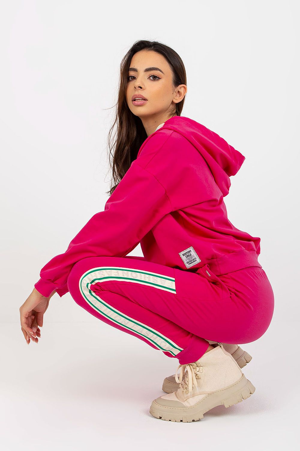 Chic model showcasing a pink cotton-blend hoodie and pants set, elegantly posed in a squat position, highlighting the set's vibrant colour and stylish design.